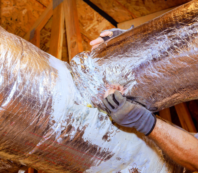Hands working on sealing ductwork in a residential attic during home maintenance task